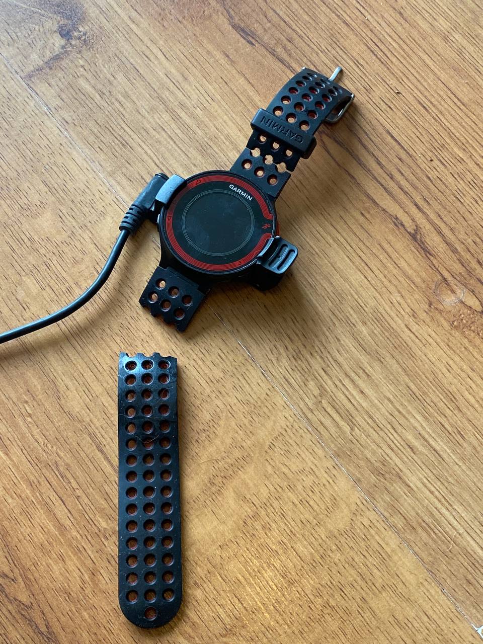 Old Garmin Forerunner on its charging cradle with one side of the wrist strap snapped off next to it