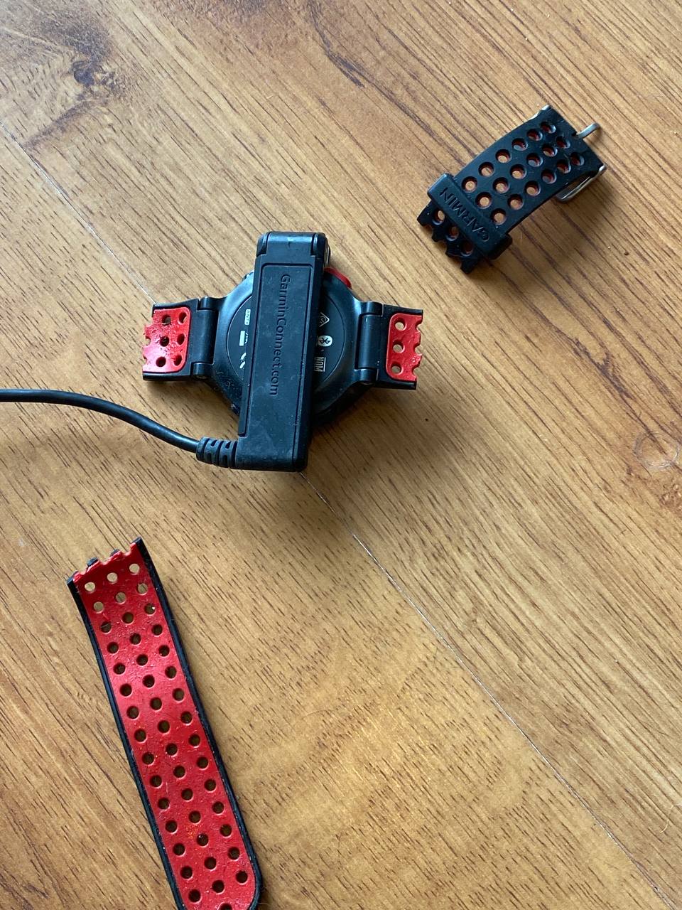 Garmin Forerunner watch face-down on a wood table with both sides of the perforated wrist strap broken off and lying nearby